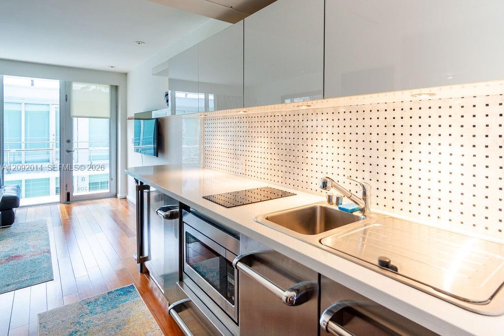 Modern condo kitchen with stainless steel appliances and a square-pattern backsplash beside sliding glass doors.