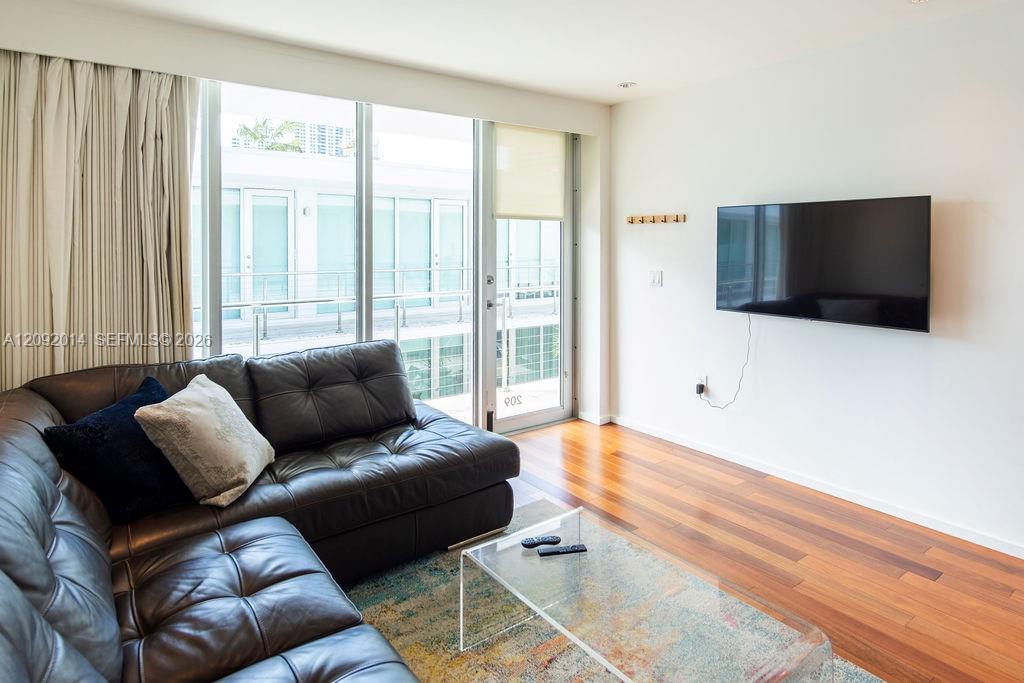 Condo living room with a dark leather sectional, hardwood floors, and sliding glass balcony doors.