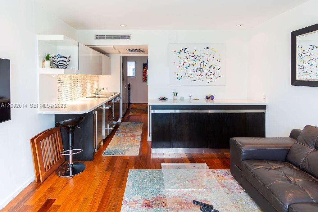 Open-plan living room and kitchen with dark cabinetry, hardwood floors, and a leather sofa.