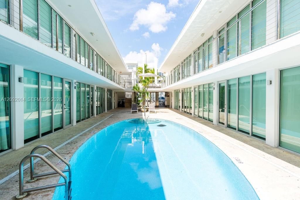 Courtyard swimming pool between modern condominium wings, with glass doors and tropical plants.