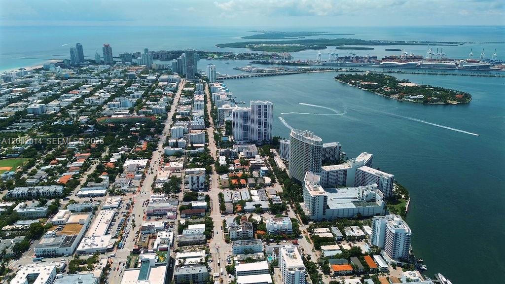 Aerial view of Miami Beach and Biscayne Bay, with high-rises, boats, and downtown Miami in the distance.