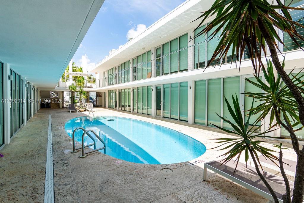 Courtyard swimming pool between modern residences, framed by glass balconies and tropical plants.