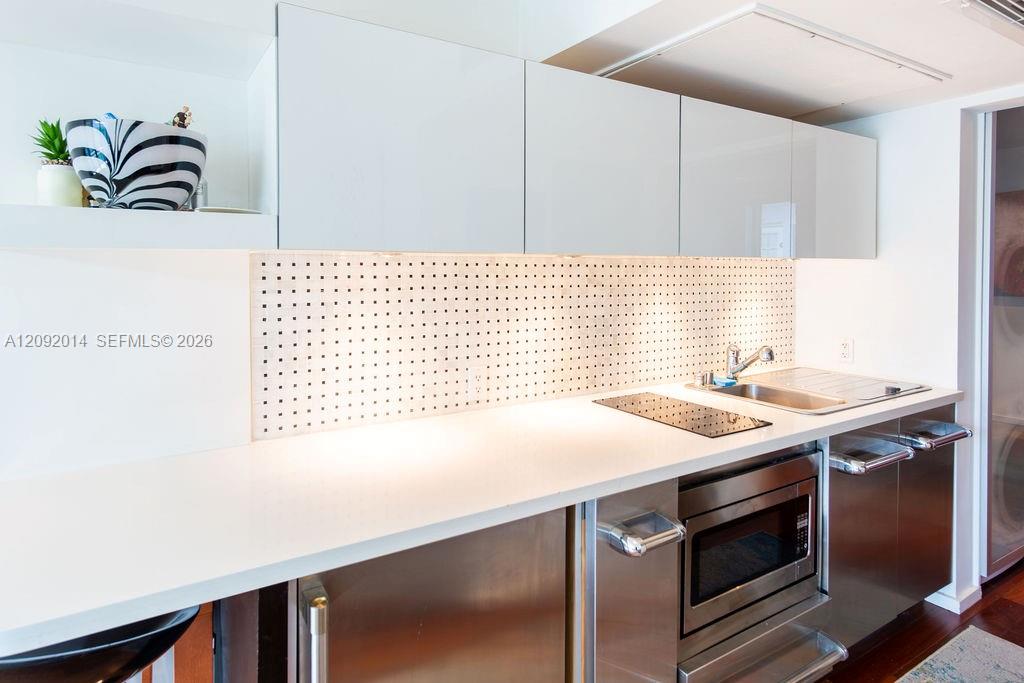 Modern kitchen with white cabinets, a long counter, perforated backsplash, and stainless-steel appliances.