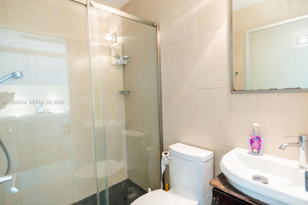 Bathroom with a glass-enclosed shower, beige tile, and a vessel sink on a dark stone vanity.