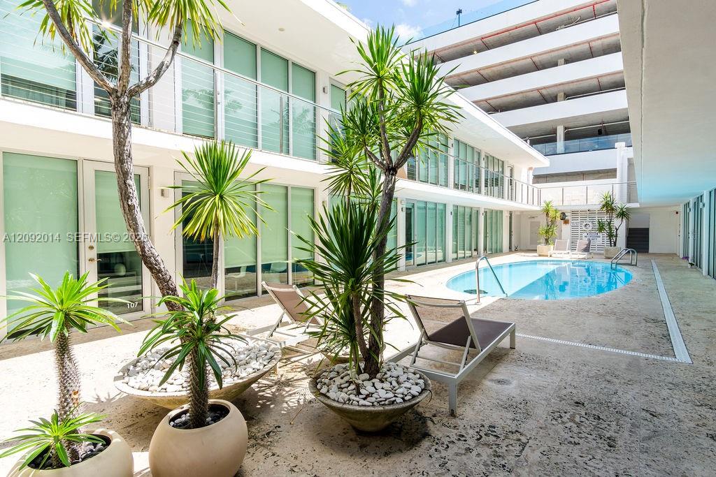 Condominium courtyard pool surrounded by tropical potted palms and lounge chairs.