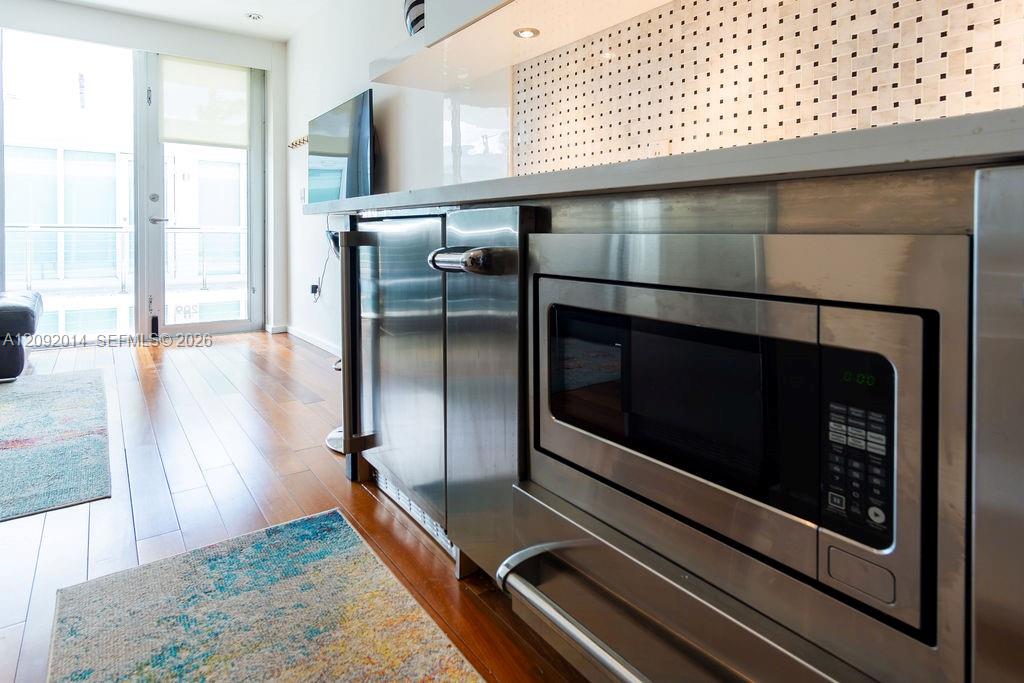 Condo kitchen with stainless steel appliances, a perforated tile backsplash, and wood floors.