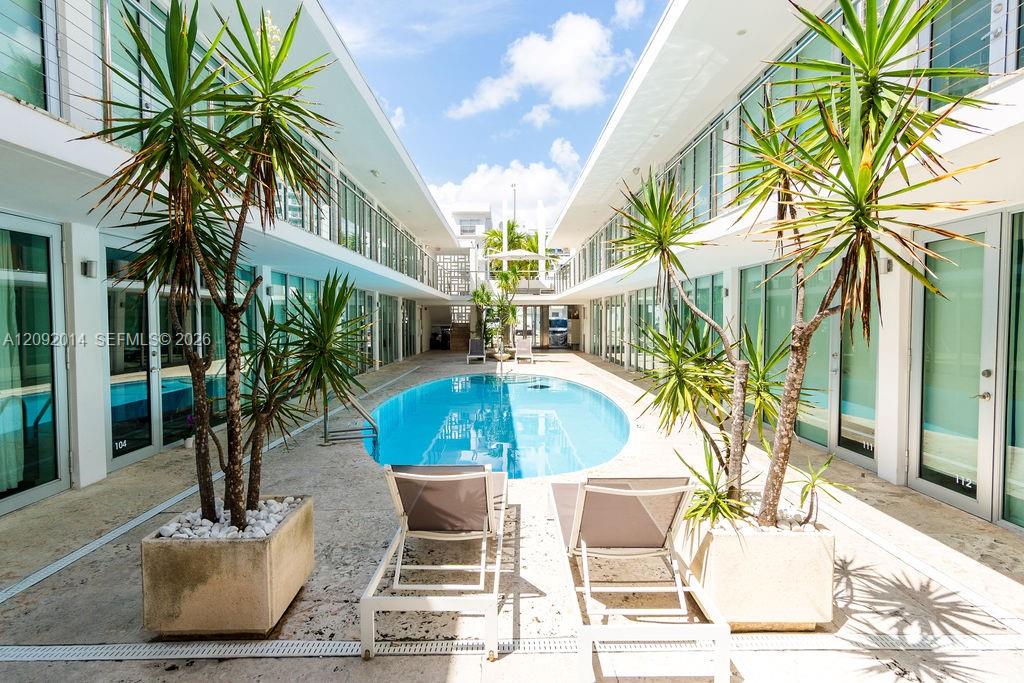 Courtyard pool between modern residences, framed by tropical plants and two lounge chairs.