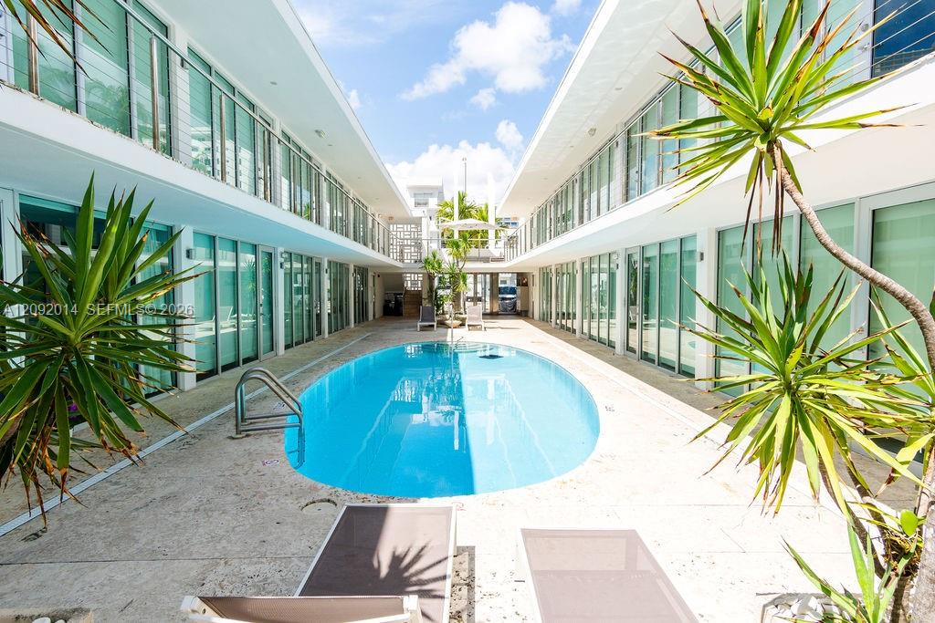 Courtyard pool between modern condo buildings, framed by tropical plants and lounge chairs.