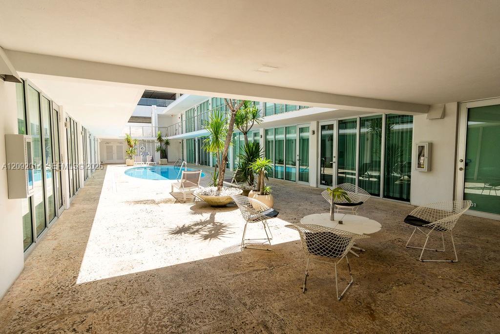 Residential courtyard with a small pool, tropical plants, and white wire-frame chairs.