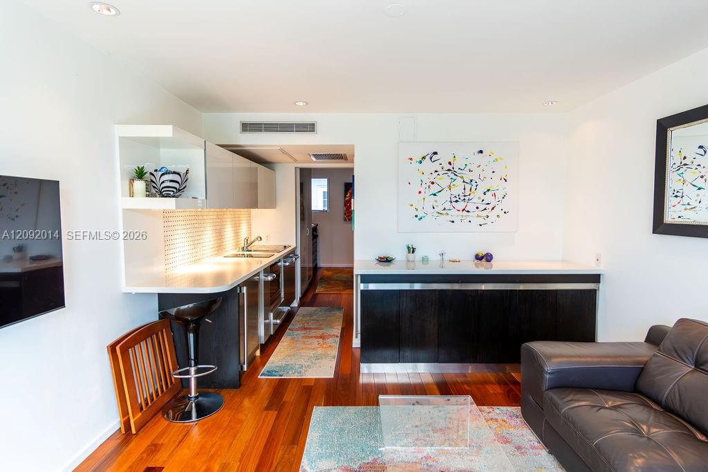 Open-plan kitchen and living area with dark cabinets, hardwood floors, and a leather sofa.
