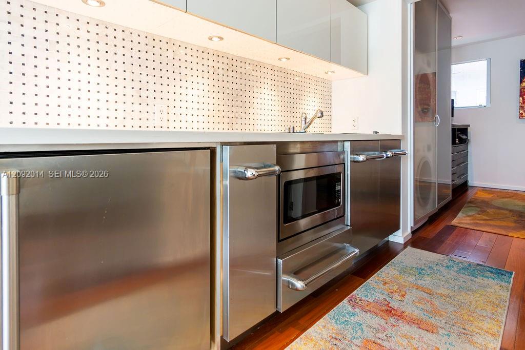 Modern kitchen with stainless steel appliances, perforated white backsplash, and colorful runner on wood floors.