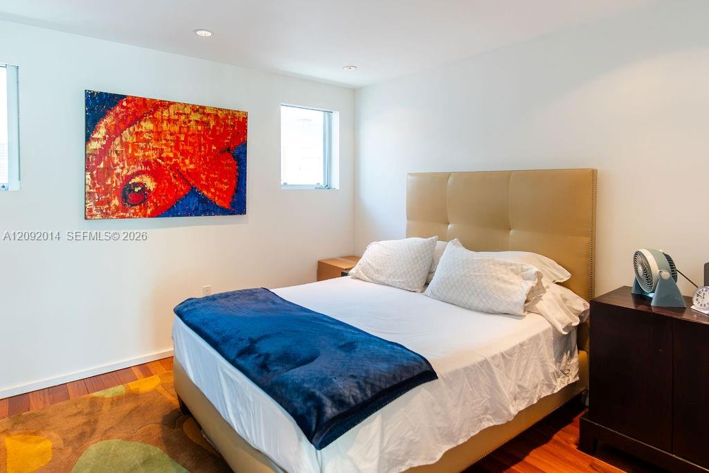 Bedroom with a tan upholstered headboard, blue bed throw, and colorful fish artwork.
