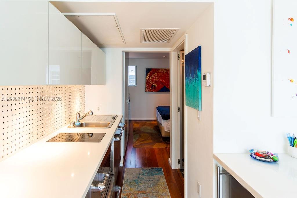 Galley kitchen with white counters and glass-front cabinets, opening toward a bedroom.