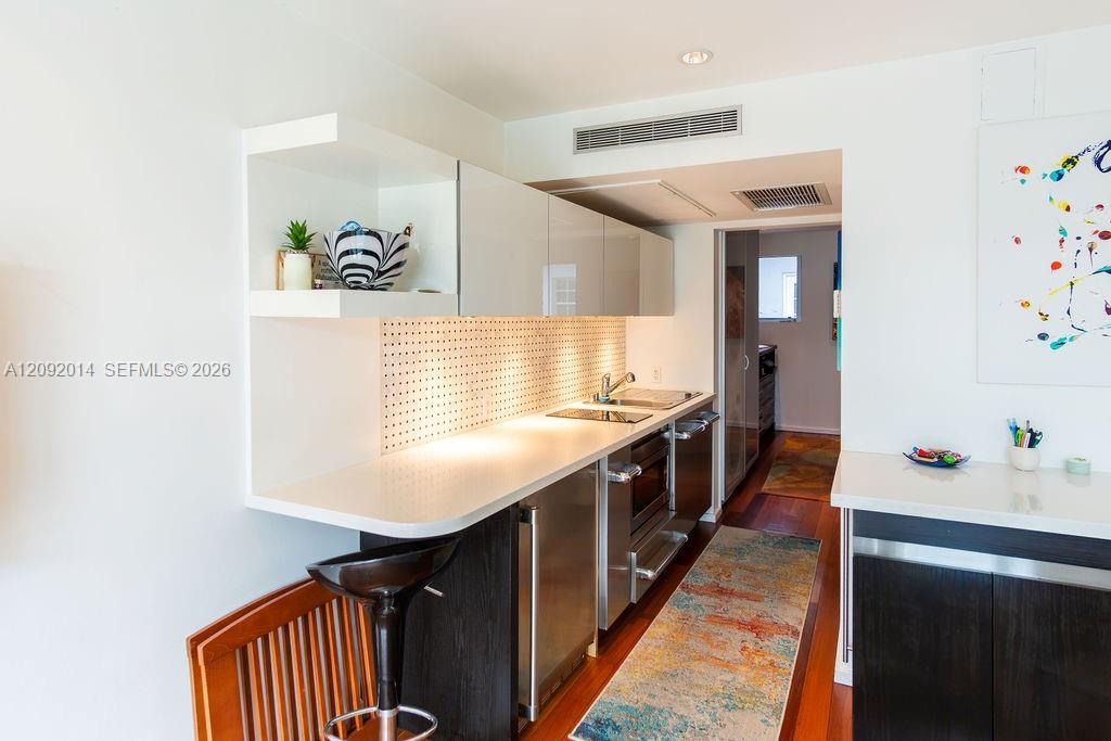 Narrow modern kitchen with white counters, stainless appliances, and dark wood cabinetry.