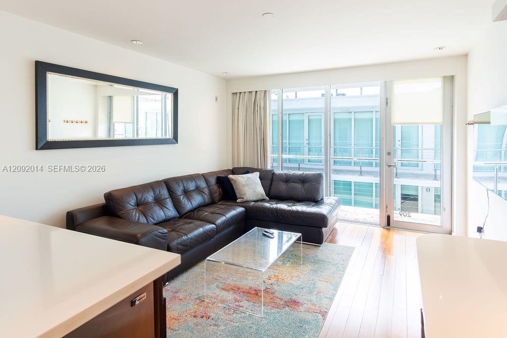 Living room with a dark leather sectional and sliding glass doors opening to a balcony.