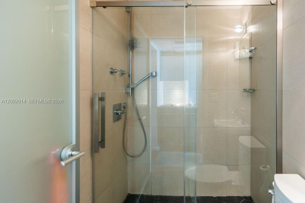 Glass-enclosed tiled shower with a handheld showerhead and dark floor.