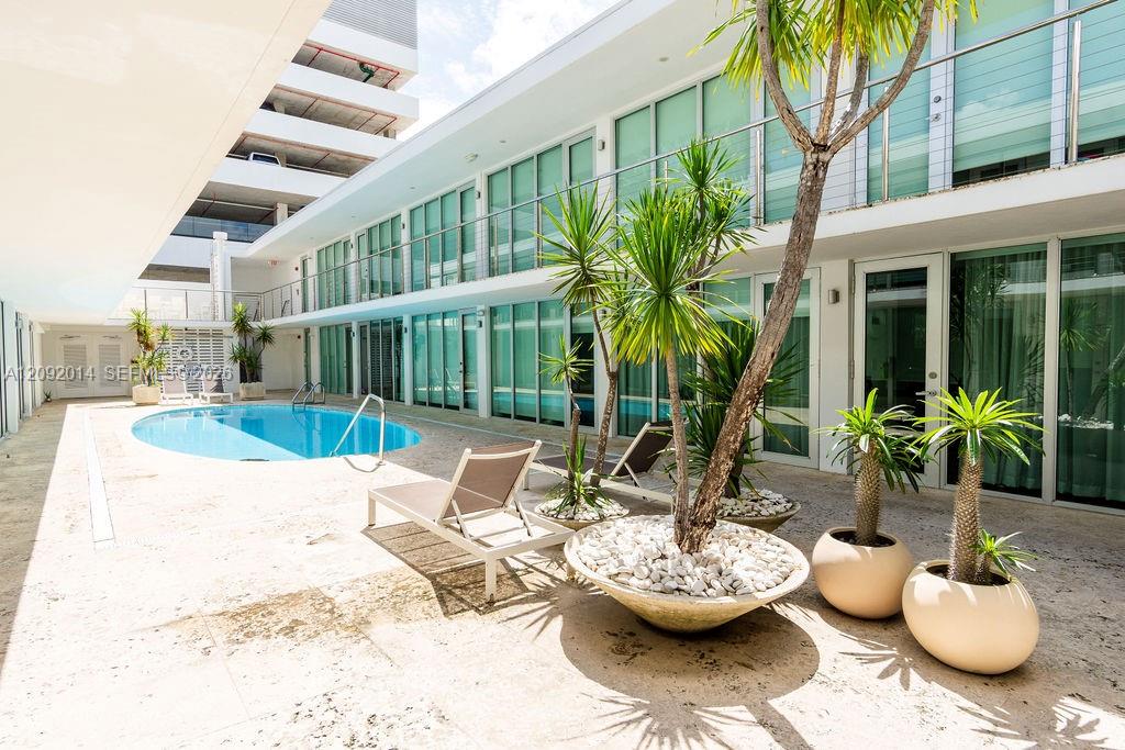 Courtyard pool beside modern residences, with lounge chairs and tropical plants.