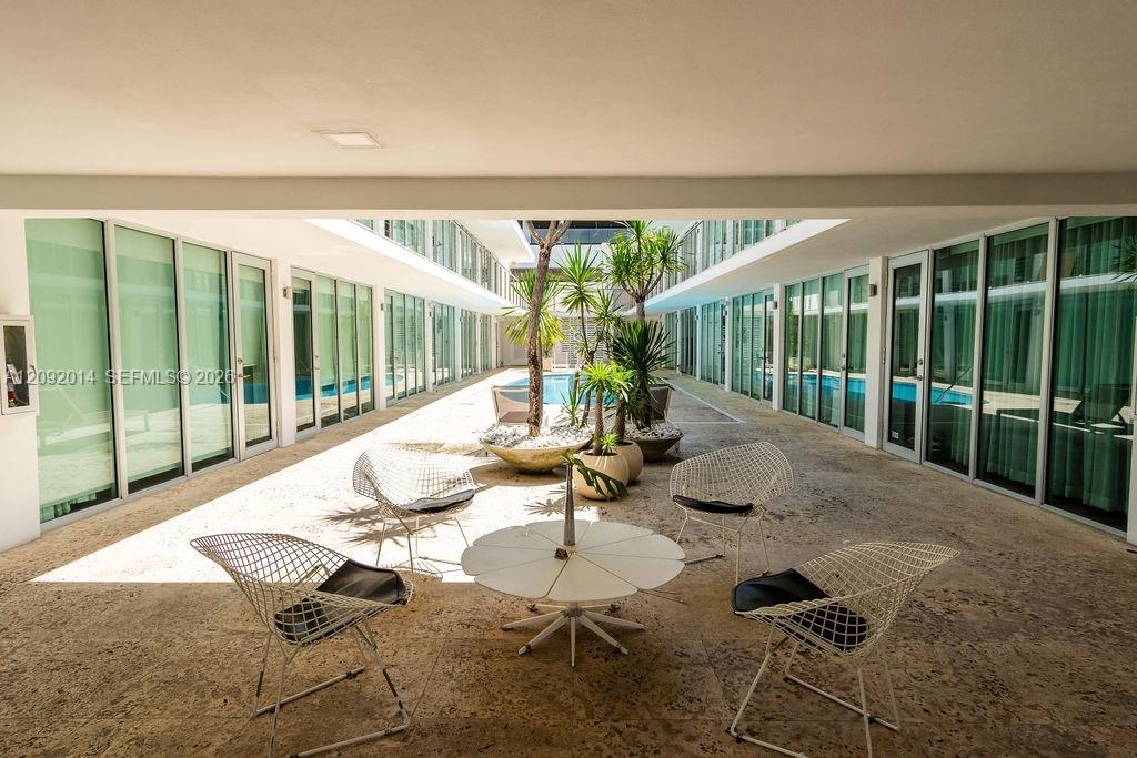 Condominium courtyard lounge with tropical plants, wire chairs, and glass-fronted units.