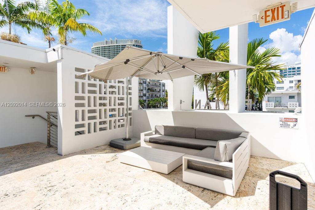 Outdoor terrace with a gray sectional and table beneath a large umbrella, surrounded by palm trees.