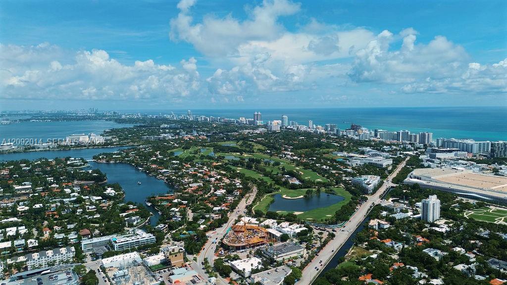 Aerial view of Miami Beach with oceanfront high-rises, waterways, and a golf course.