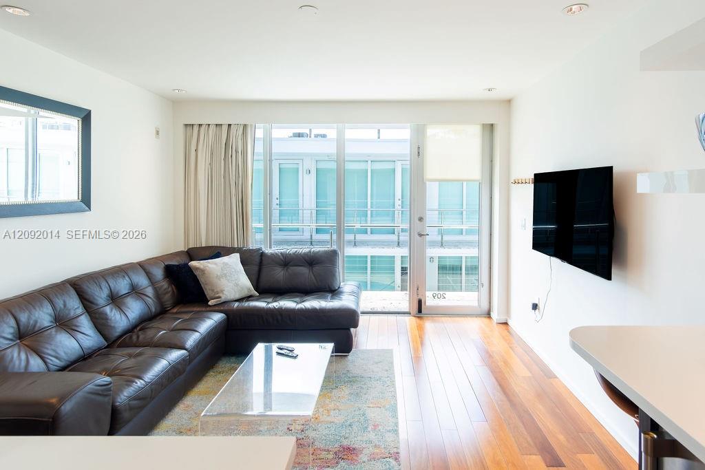Furnished living room with a leather sectional, colorful rug, and sliding doors to a balcony.