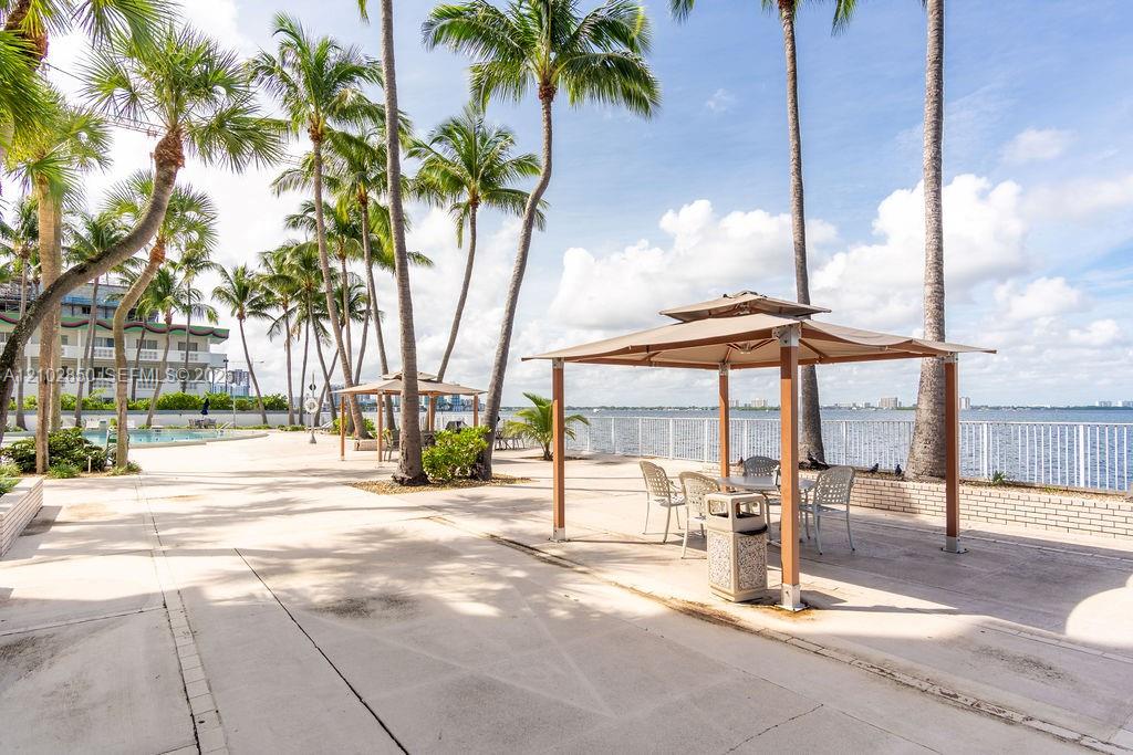Waterfront condo patio with palm trees, shaded seating, a pool, and views across the bay.