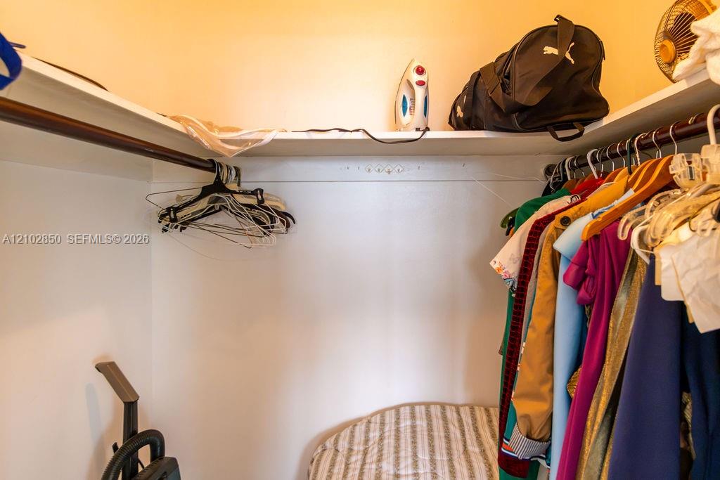 Bedroom closet with hanging clothes, wire hangers, a shelf, and an ironing board.