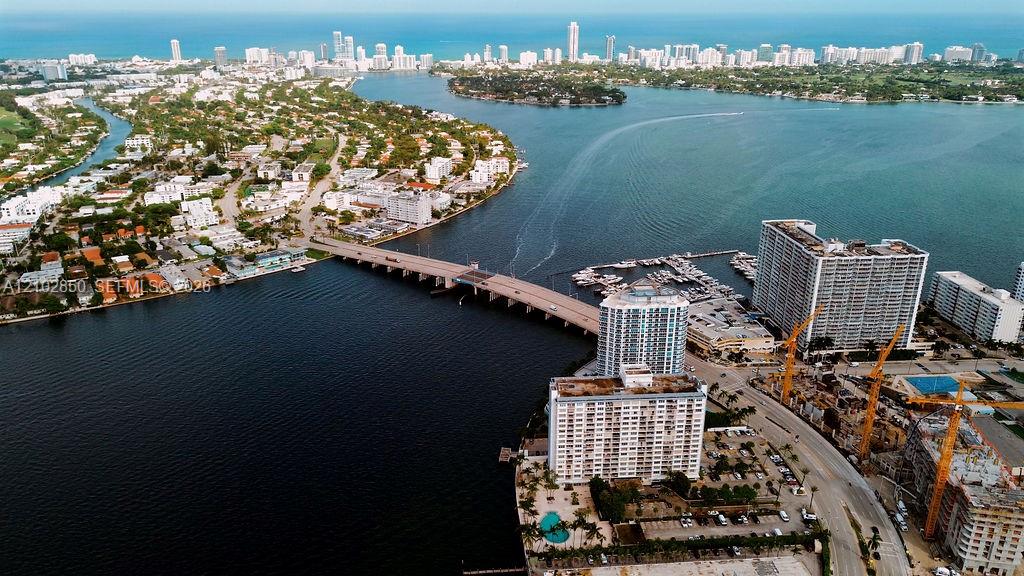 Aerial waterfront view with a bridge, marina, high-rises, and distant city skyline.