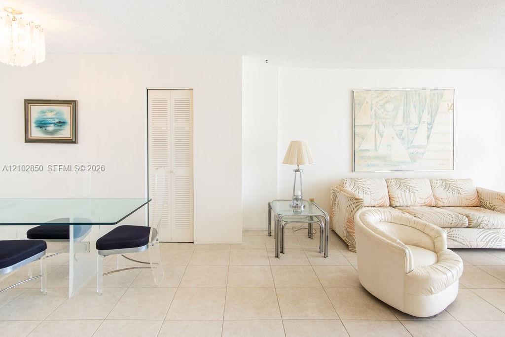Living and dining area with a glass table, cream sectional, tiled floor, and coastal artwork.