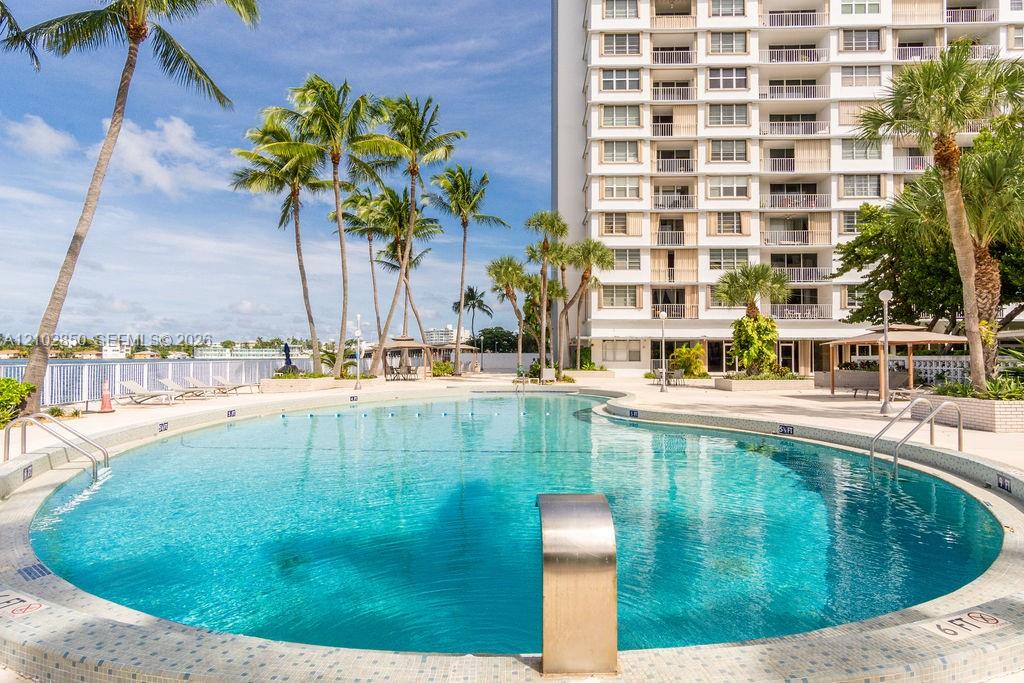 Outdoor condominium pool with a curved edge, palm trees, and a tall apartment building.