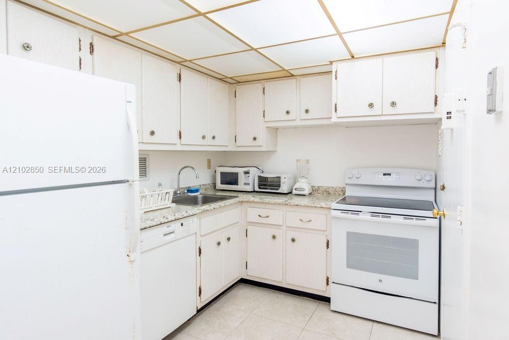 Compact white kitchen with gold-trimmed ceiling, speckled counters, and white appliances.