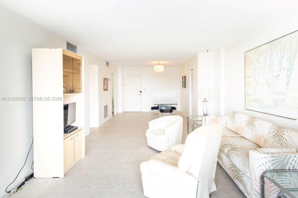 Furnished living room with a patterned sofa, white armchairs, pale tile floors, and large abstract wall art.