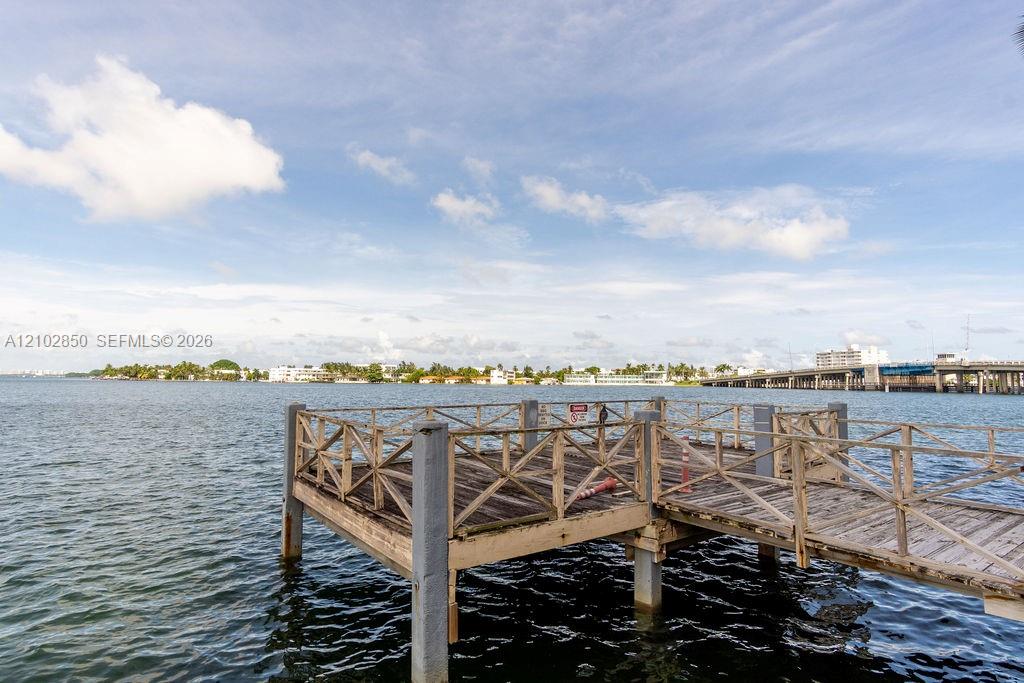 Wooden dock over bay water, with a bridge and distant shoreline.