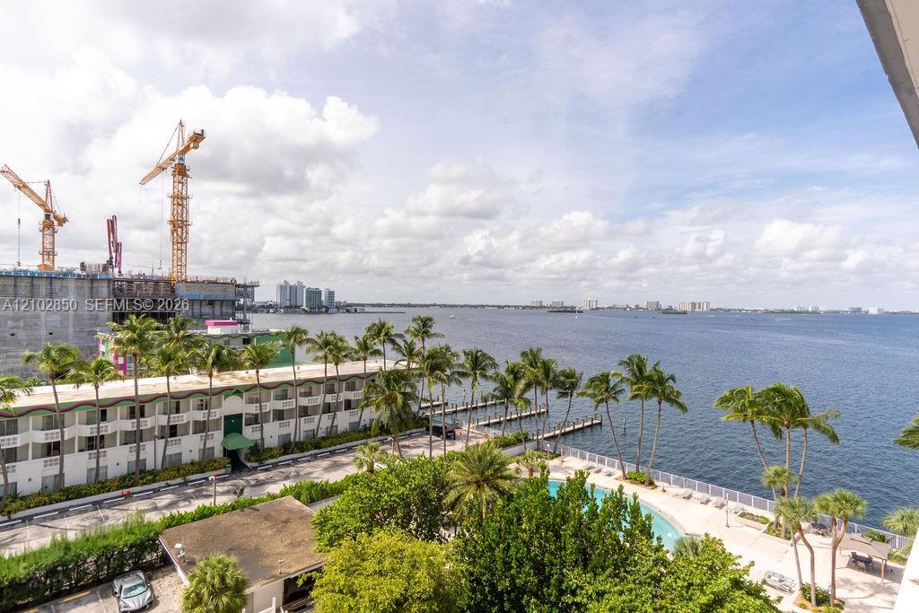 Waterfront bay view from above, with a palm-lined pool deck and construction cranes across the water.