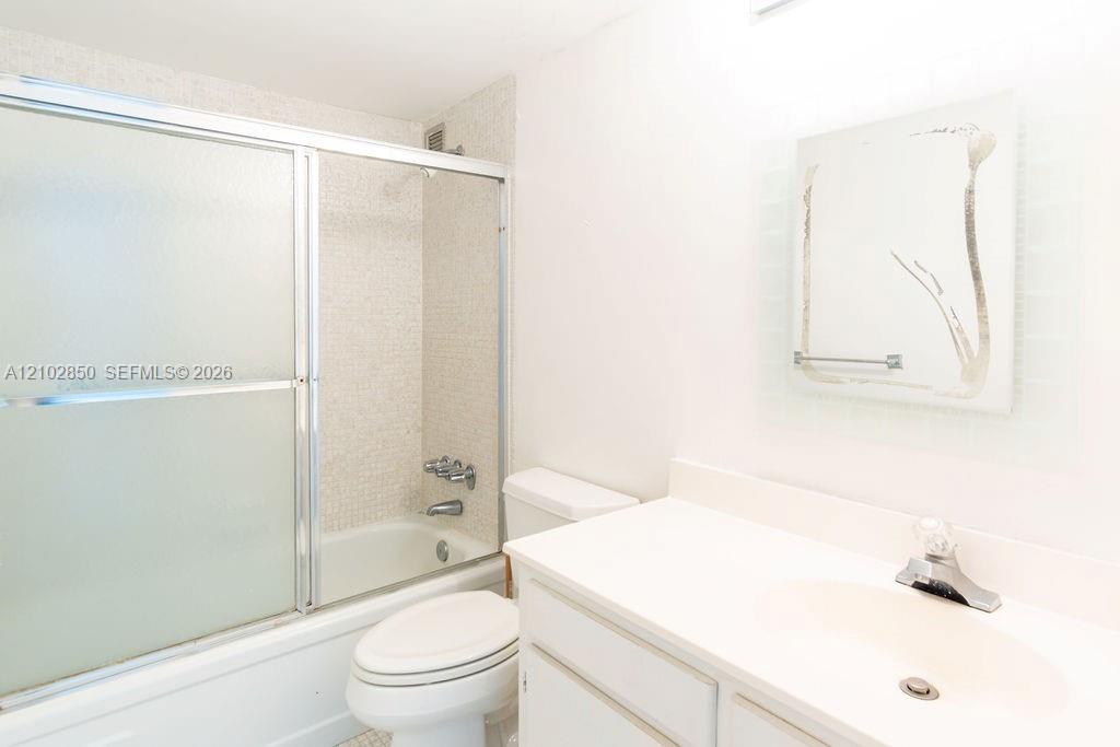 Bathroom with a frosted-door tub and shower beside a white vanity and toilet.
