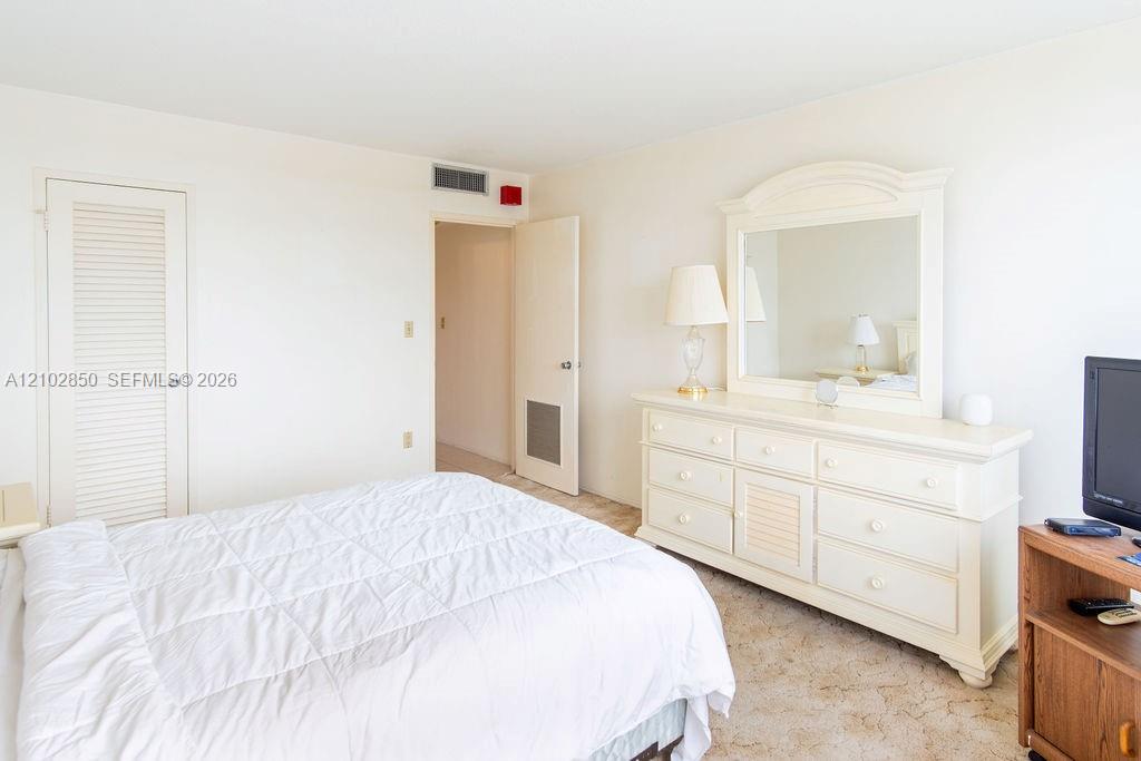 Bedroom with a white bed, cream dresser and mirror, and television.