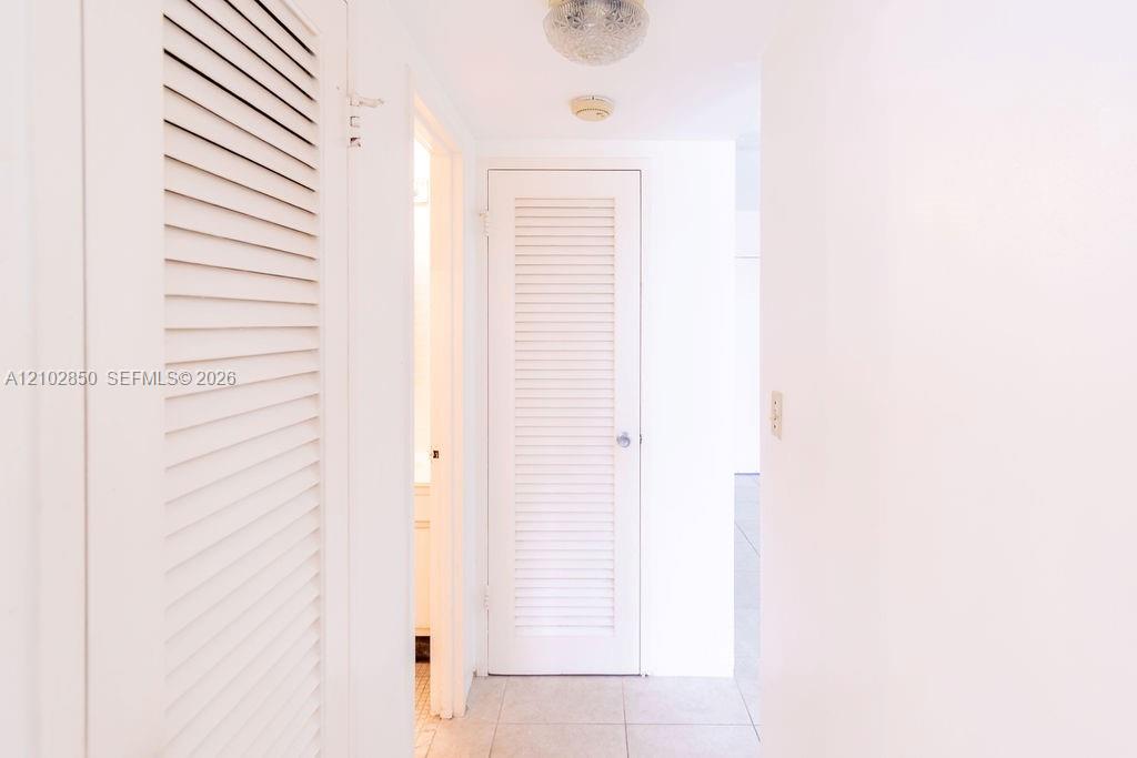 Bright hallway with white louvered doors and pale tile flooring.