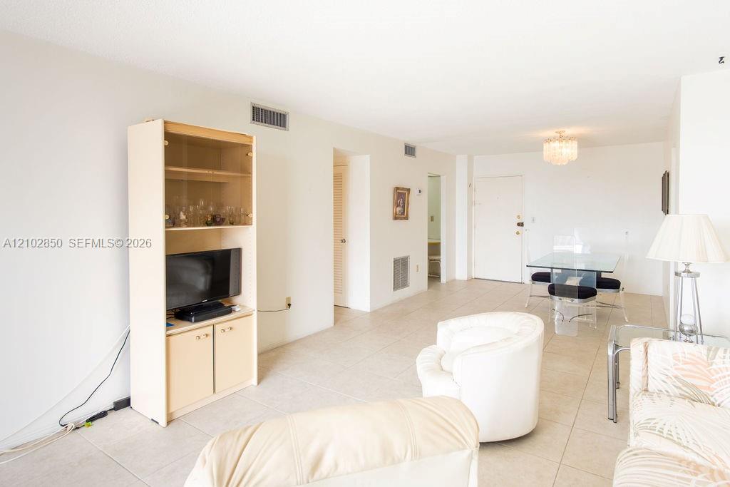 Living and dining area with white seating, tiled floors, and a glass dining table.