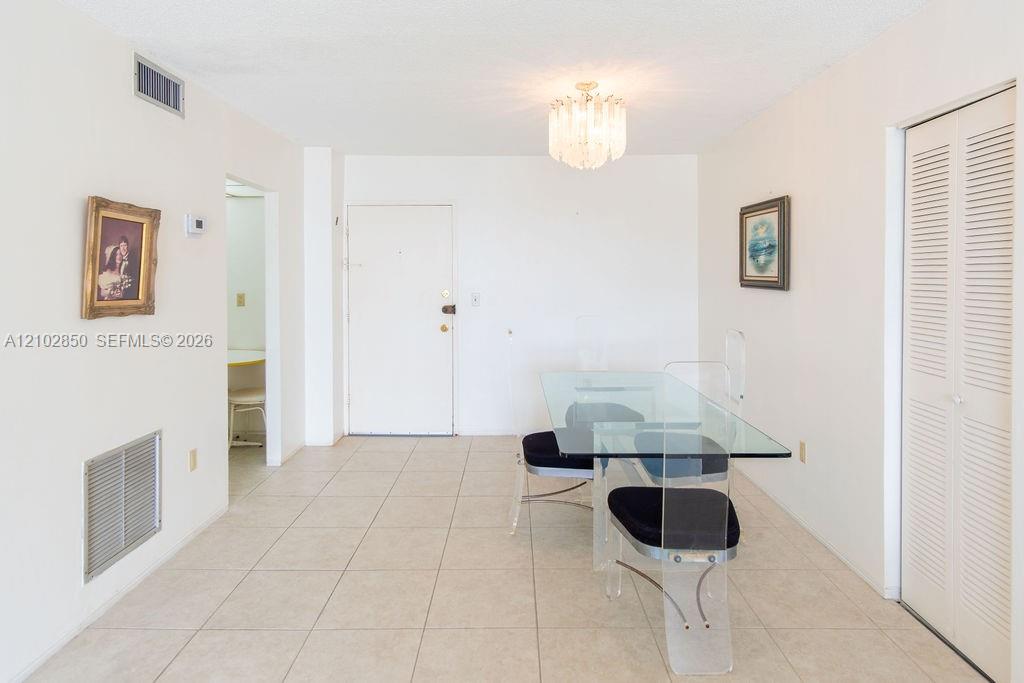 Condo dining area with a glass table, tiled floor, and chandelier.