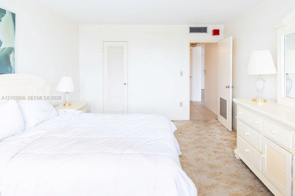Bedroom with a large white bed, matching dresser, and beige carpet.