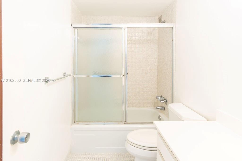 Bathroom with a white tub, frosted sliding shower doors, toilet, and vanity.