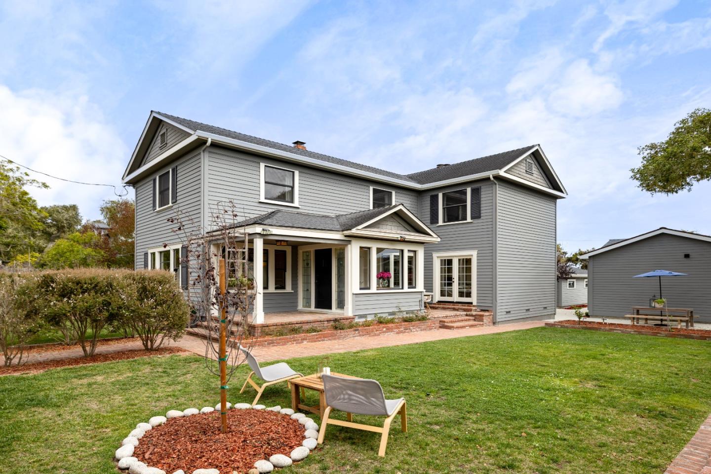 Gray two-story home with a covered patio, brick paths, and a green lawn.