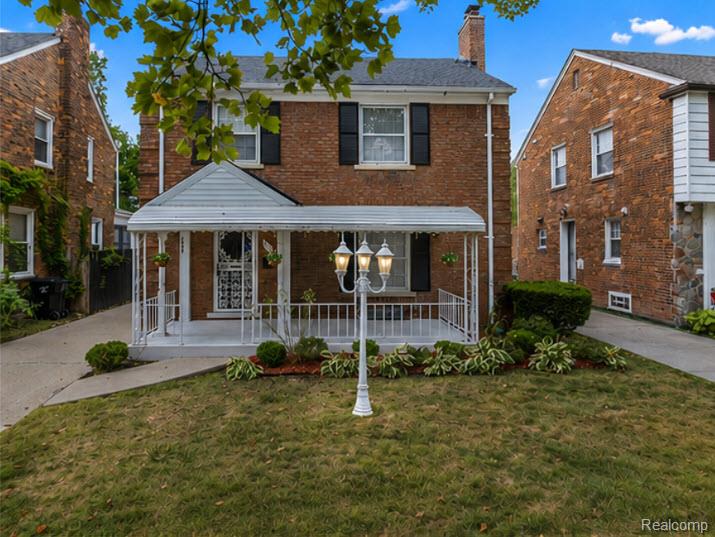 Two-story brick house with a covered white-railed porch and a lamppost in the front lawn.