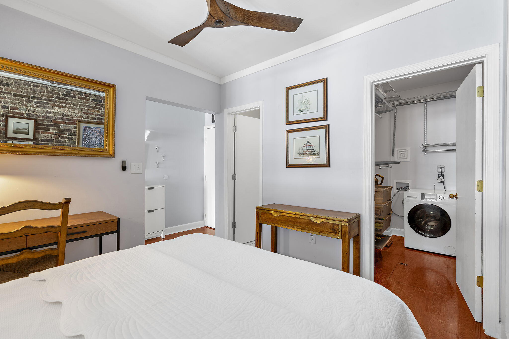 Bedroom with a white bed and wooden furniture, opening to a laundry closet with a front-loading washer.