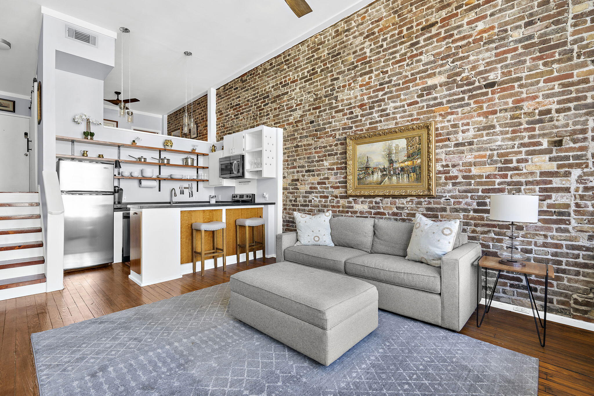 Open-plan living room and kitchen with an exposed brick wall, gray sofa, and breakfast bar.