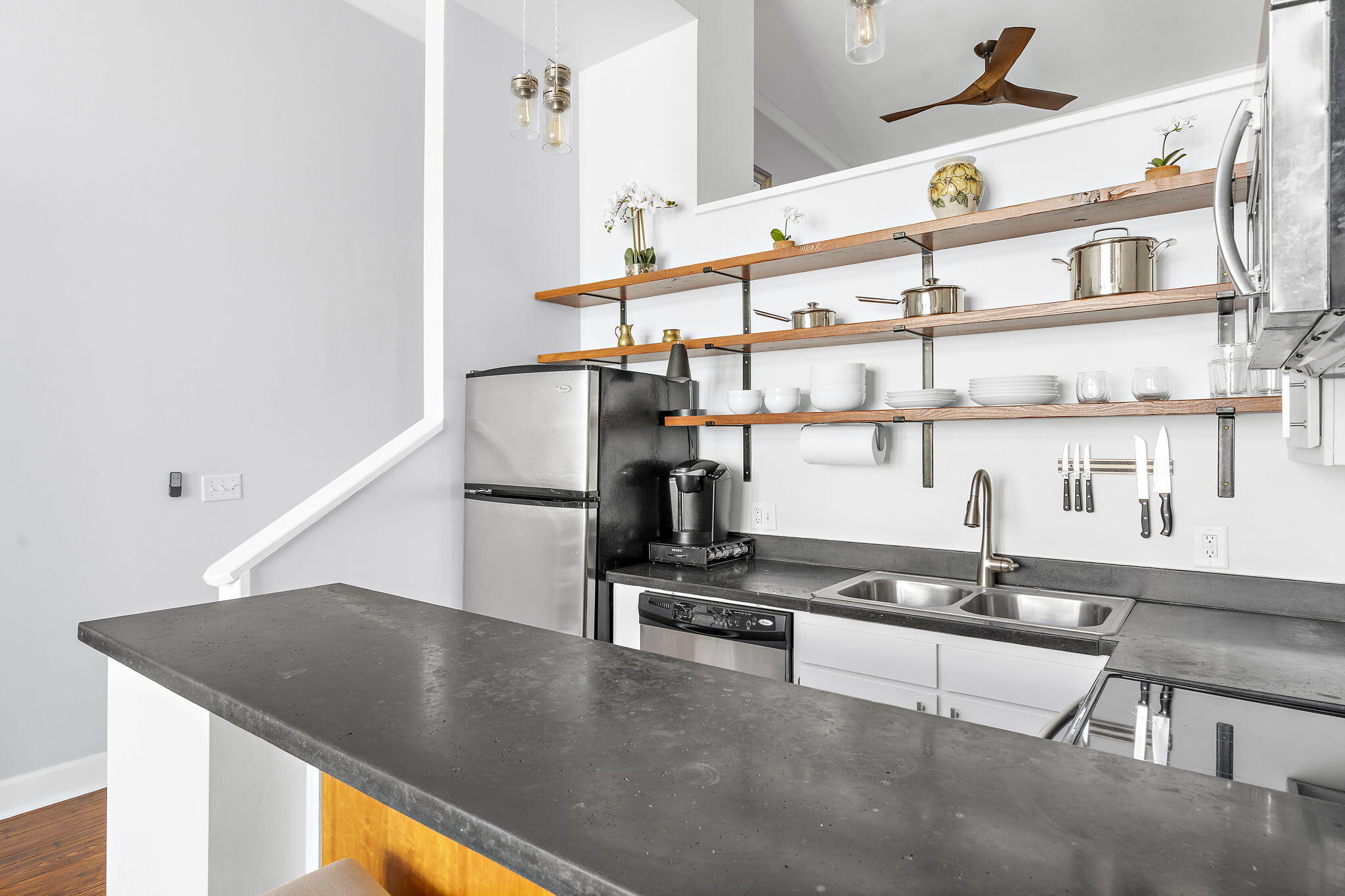 Modern kitchen with a broad dark island, stainless appliances, and long open wood shelves.