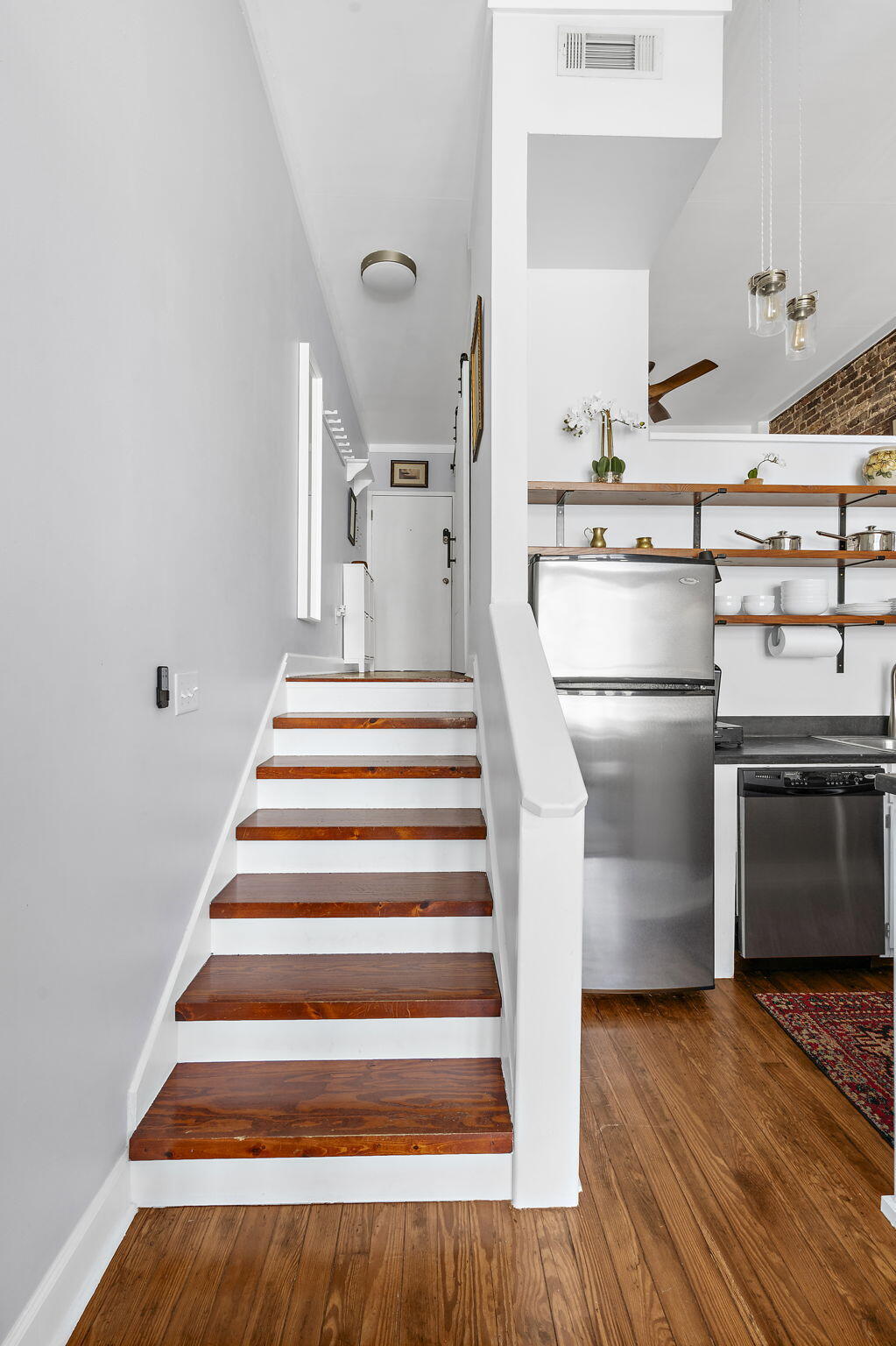 Wood-tread staircase beside a compact kitchen with stainless steel appliances and open shelving.