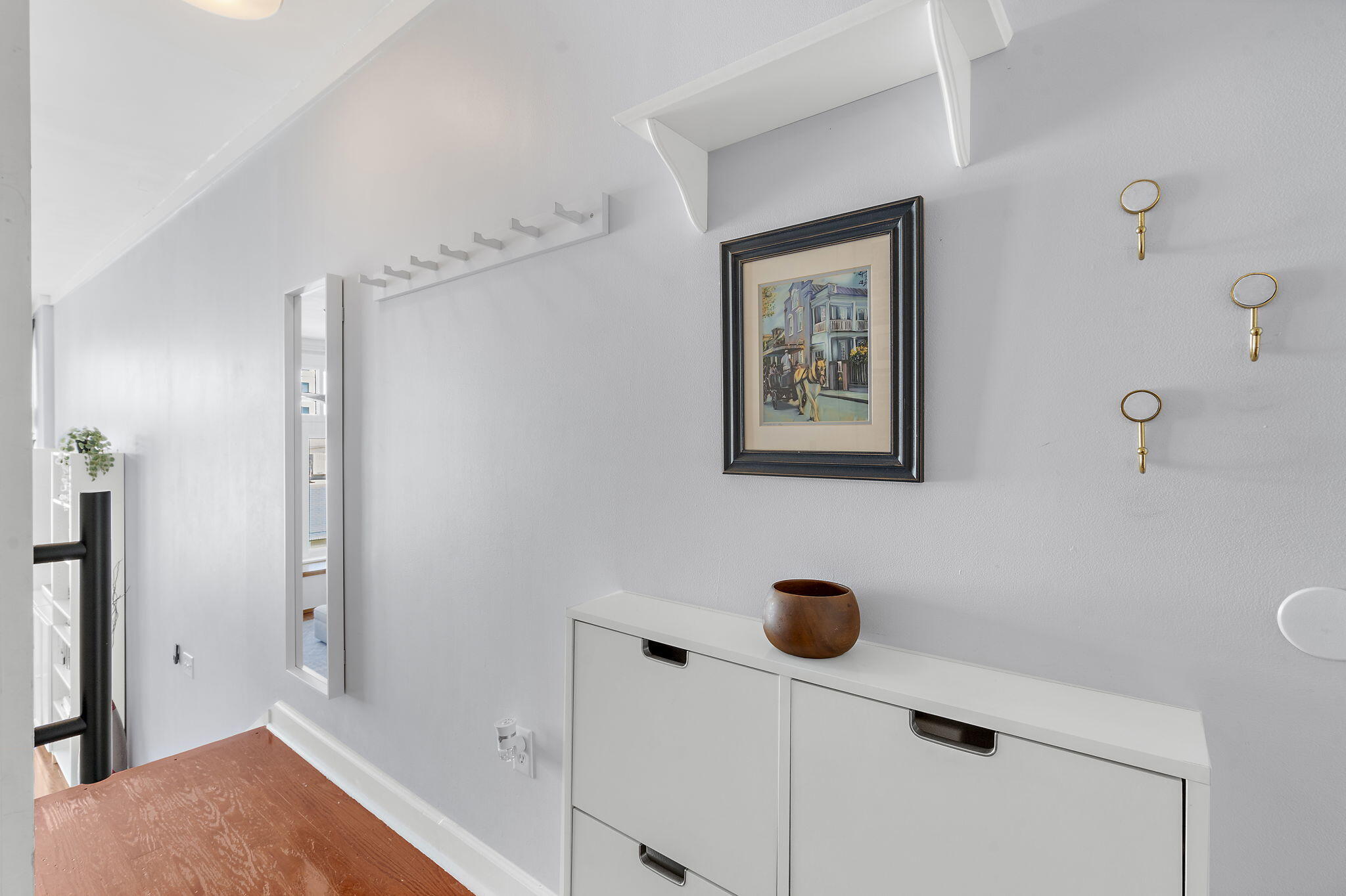 Bright hallway with white built-in storage, framed artwork, brass hooks, and warm wood flooring.
