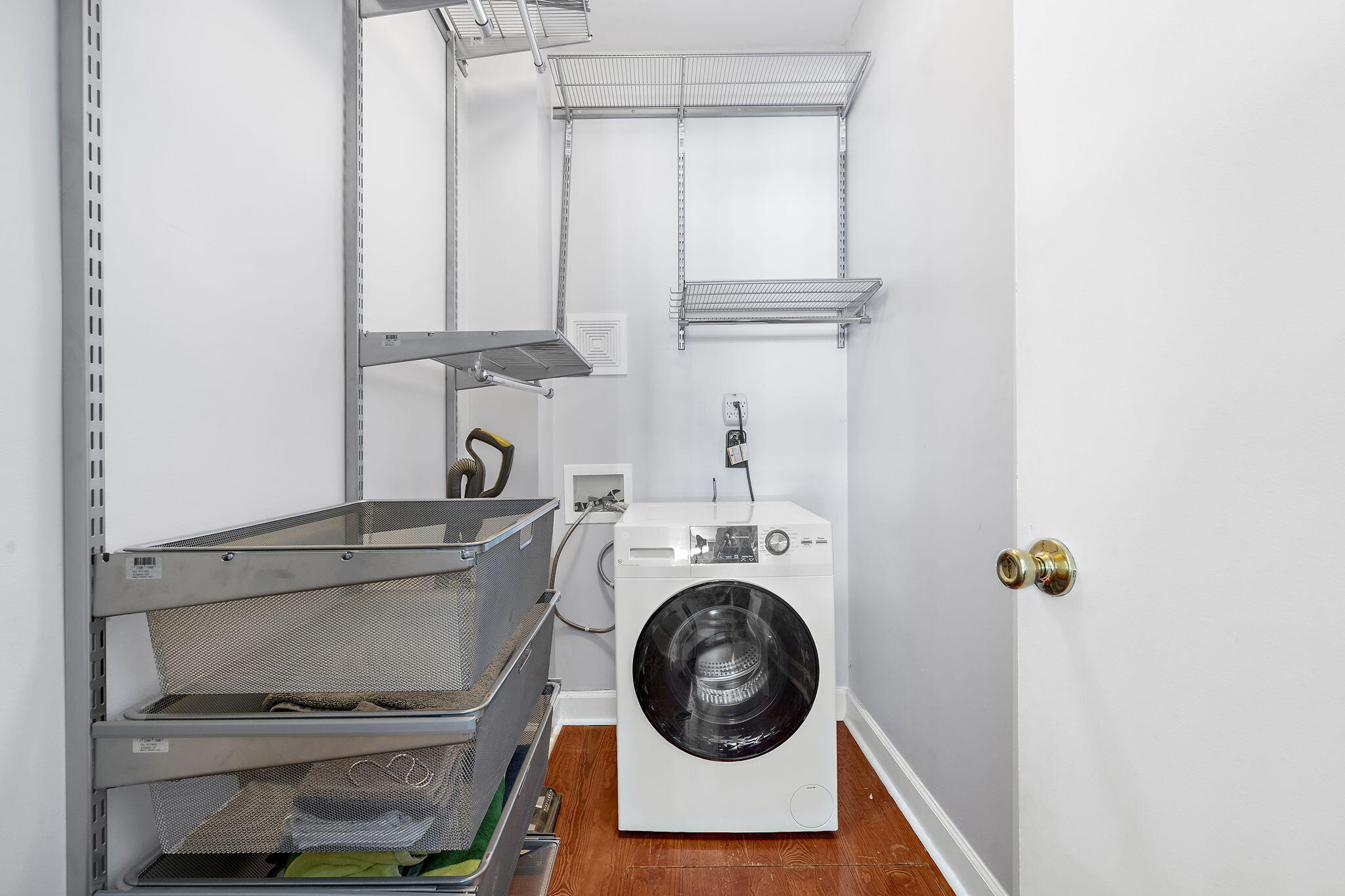 Laundry room with a front-loading washer, wire shelves, and pull-out mesh storage baskets.