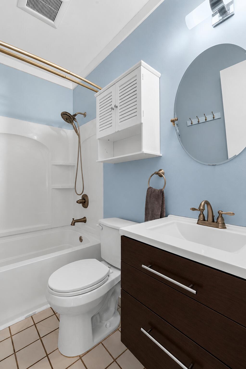 Bathroom with a white tub, dark wood vanity, round mirror, and light blue walls.